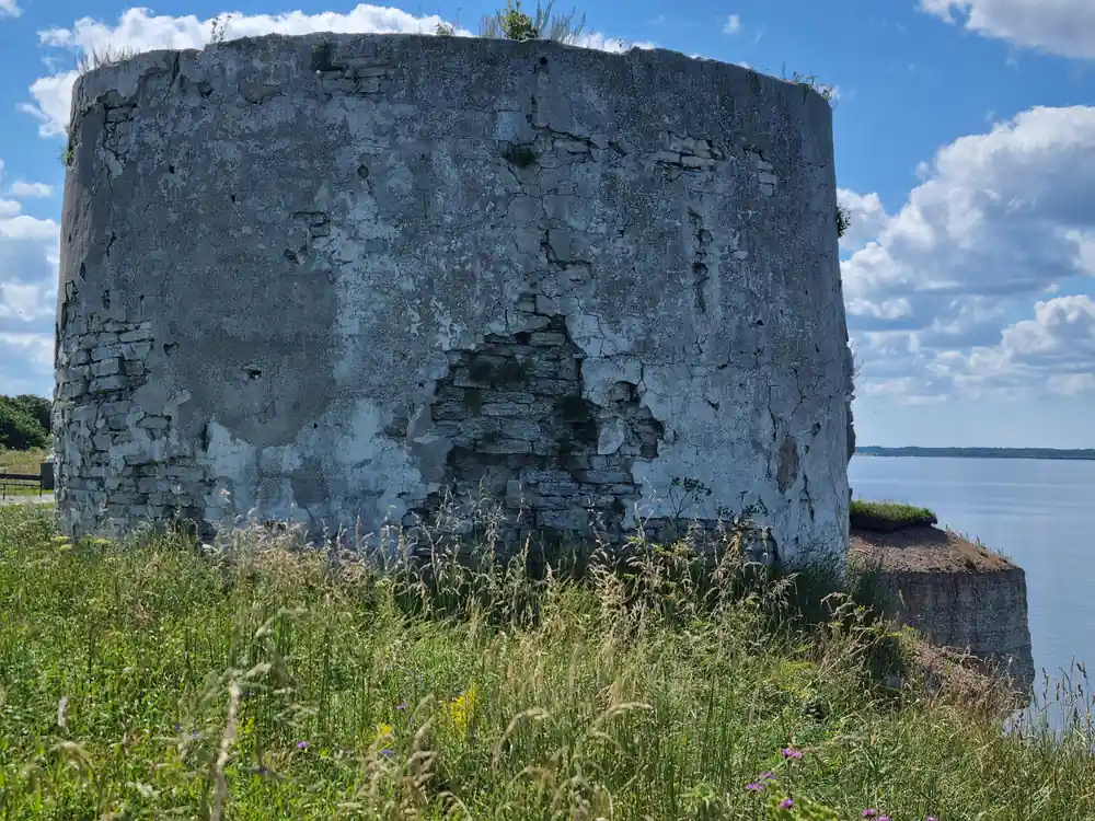 Cylindrical concrete tower ruin on grassy bank by water