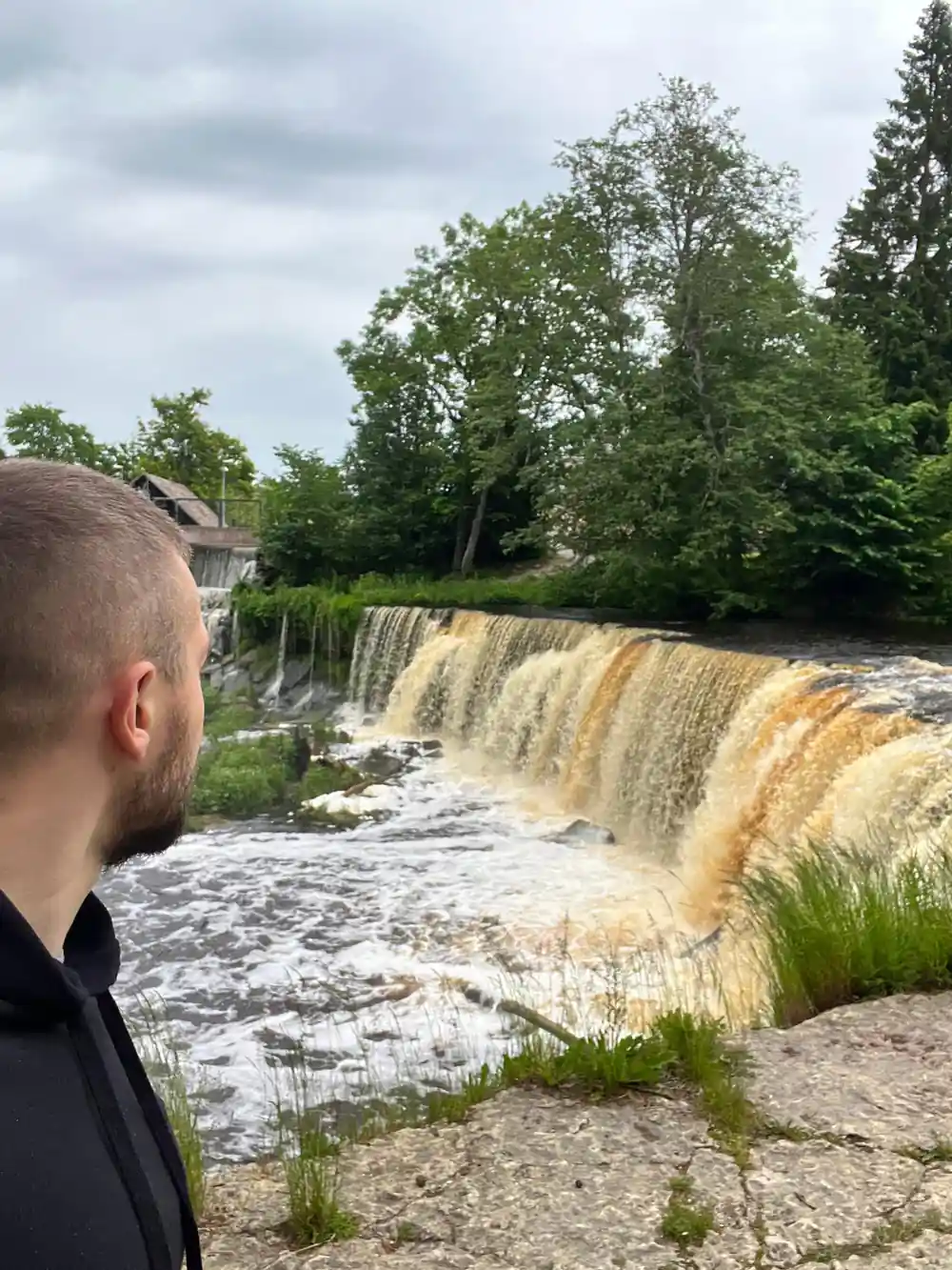 Man looking at wide waterfall cascade over stone ledge