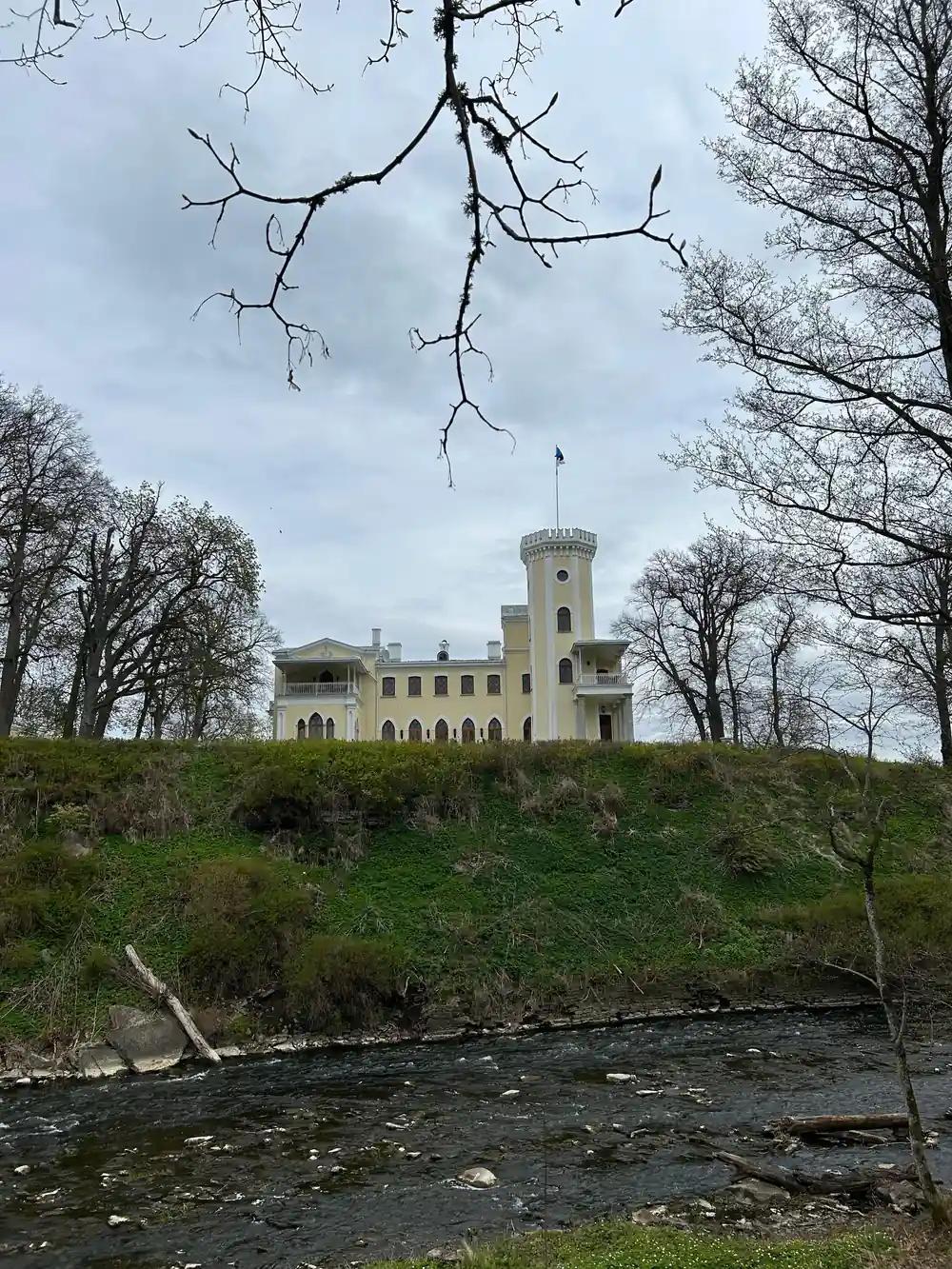 Pale castle tower on hillside above flowing river
