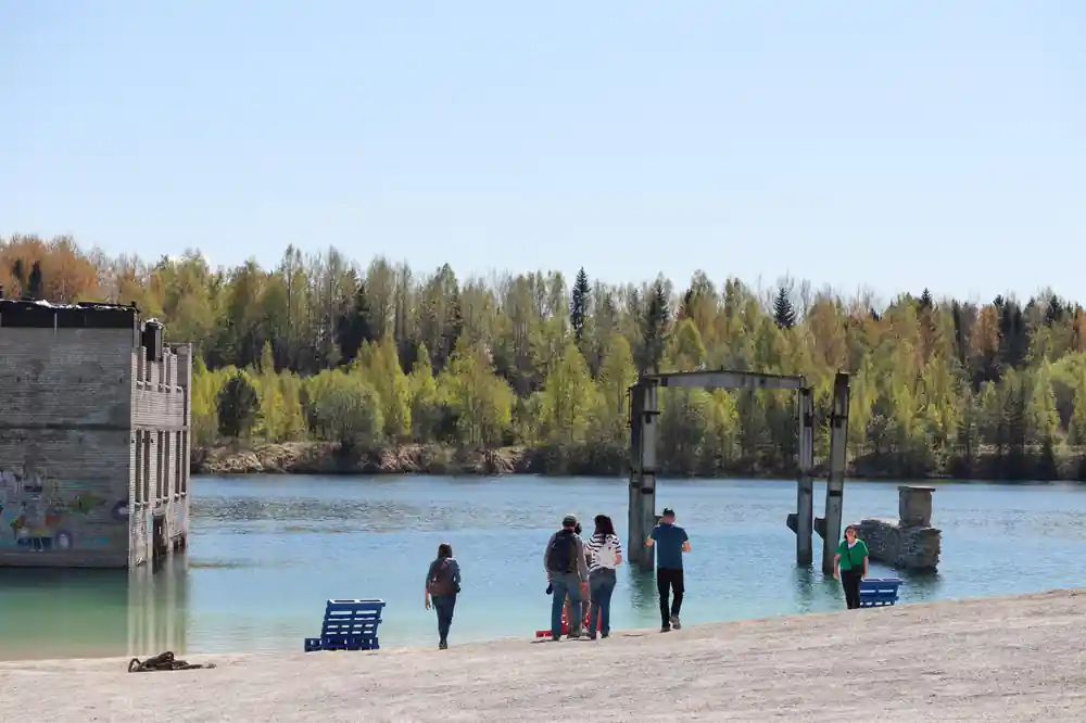 People on sandy beach by lake with forest backdrop