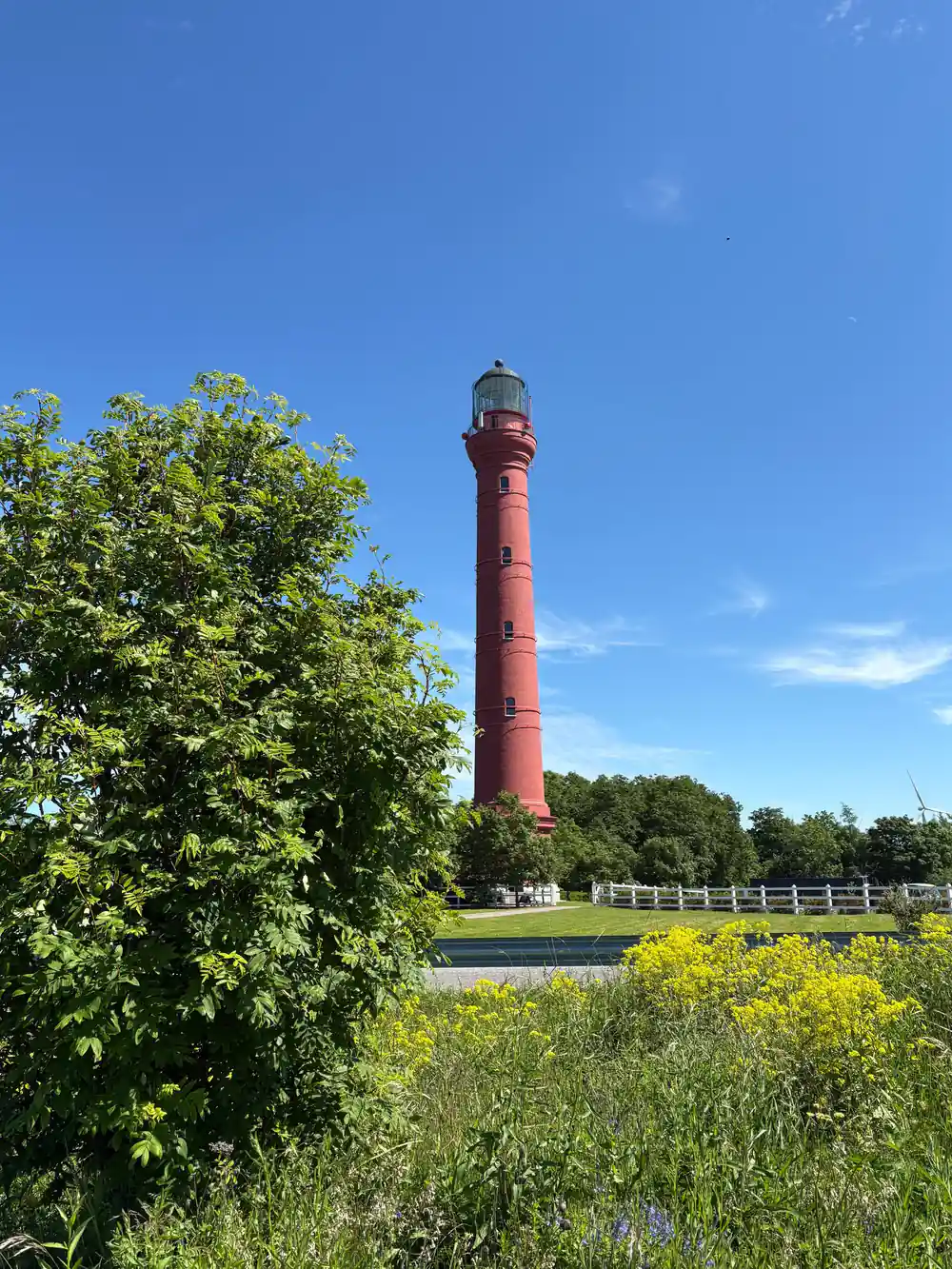 Red lighthouse tower in flat green landscape near water