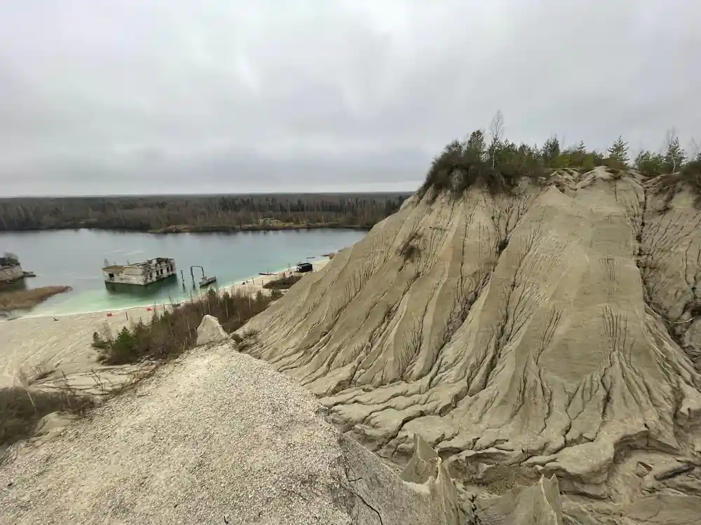 Steep sand cliff with quarrying operations and turquoise lake
