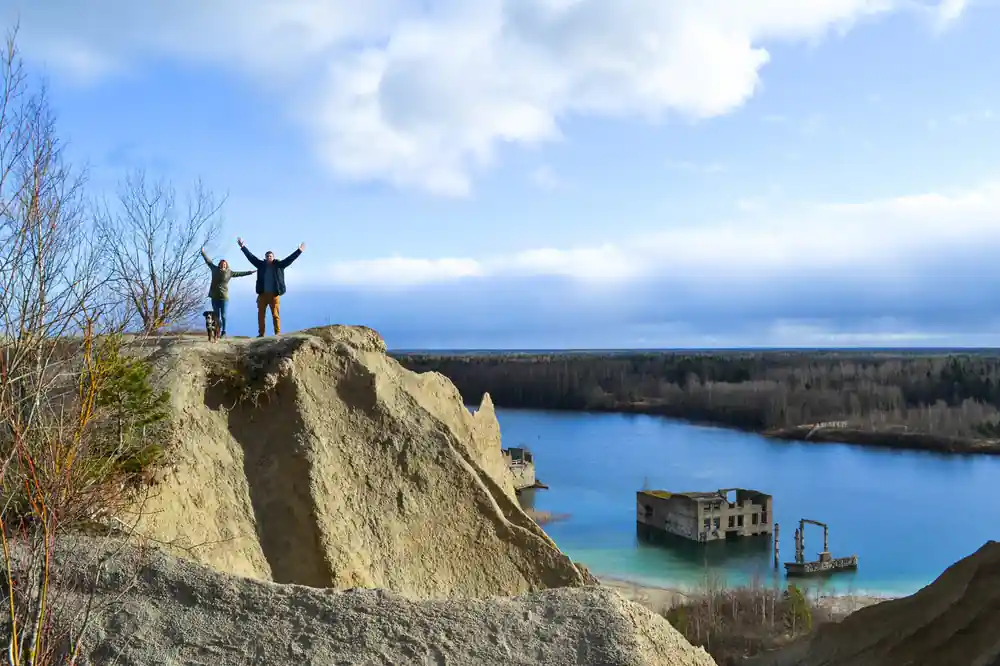 Two people with arms raised on sandy cliff overlooking quarry